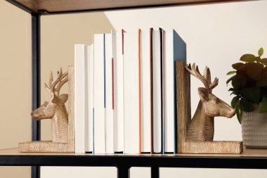 Wooden deer shaped bookends with books and plant on shelf indoors clipart
