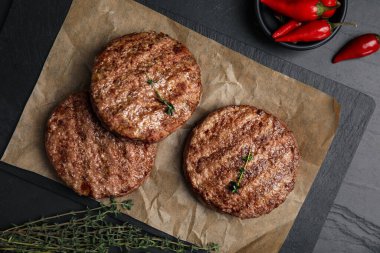 Lezzetli ızgara hamburger köfteleri, kekik ve kırmızı biberler siyah masada, düz yerde.
