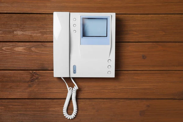 Modern intercom system with handset on wooden background, top view