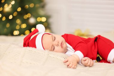 Noel kostümlü şirin bir bebek, bulanık ışık altında örülmüş battaniyede uyuyor. Kış tatili