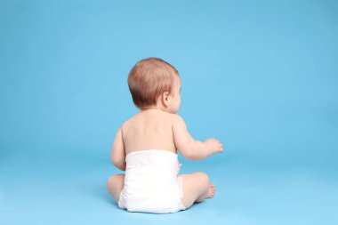 Bebek bezli şirin bir bebek açık mavi arka planda oturuyor.