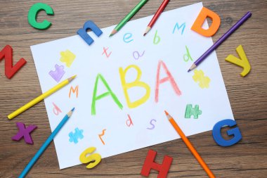 ABA (Uygulamalı davranış analizi) kısaltmalı kağıt yaprak, tahta masa üzerinde plastik harfler ve kalemler, düz yatıyordu