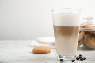 Lezzetli latte macchiato, kurabiyeler ve kahve çekirdekleri beyaz mermer masada, mesaj için yer var.