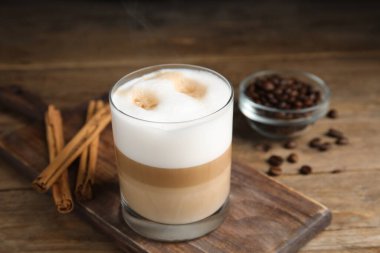 Lezzetli latte macchiato, tarçın çubukları ve ahşap masada kahve çekirdekleri.