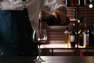Barmen, kapalı mekanda bardağa kırmızı şarap dolduruyor.