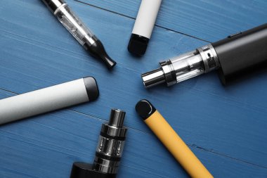 Mavi ahşap arka planda farklı elektronik sigaralar.