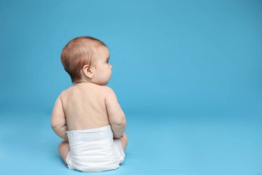 Açık mavi arka planda oturan bebek bezi takmış şirin bir bebek. Metin için boşluk