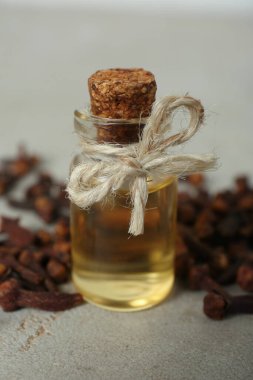 Temel yağ ve kurutulmuş karanfiller açık gri masada, yakın plan.