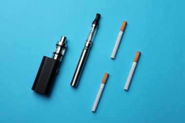 Açık mavi arka planda elektronik ve normal sigaralar, düz uzanma