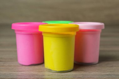Renkli oyun hamuru olan plastik kaplar ahşap masada, yakın plan.