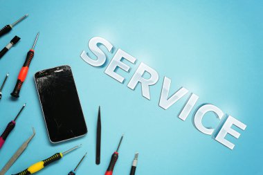 Açık mavi arkaplanda hasarlı akıllı telefon ve tamir aracı, düz yatar