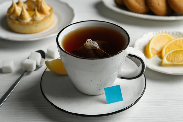 白い木のテーブルの上にお湯とレモンのカップにティーバッグ — ストック写真