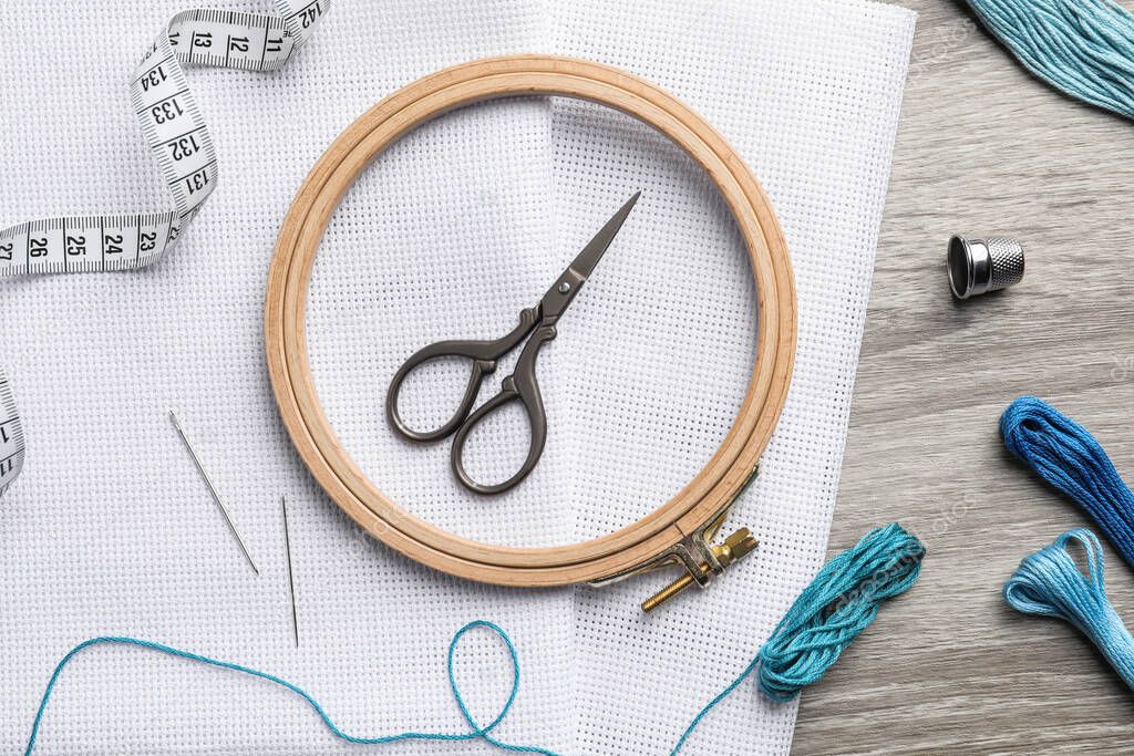 Embroidery hoop, fabric and other accessories on wooden table, flat lay