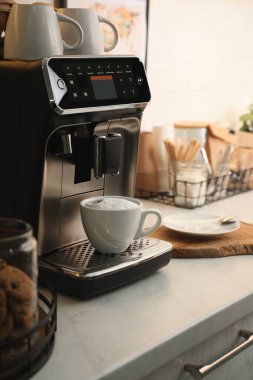 Mutfakta bir fincan kapuçino ile modern kahve makinesi.