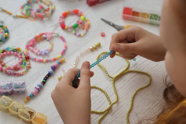 Beyaz ahşap masada boncuklu mücevher yapan kız, yakın plan.