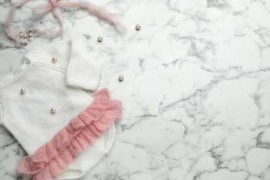 Beyaz mermer arka planda şirin örülmüş bebek tulumu, üst manzara. Metin için boşluk