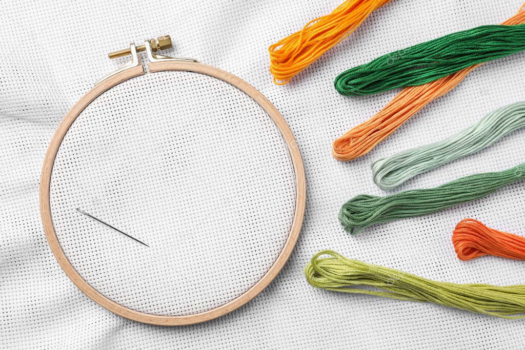 Threads near embroidery hoop with white fabric, flat lay