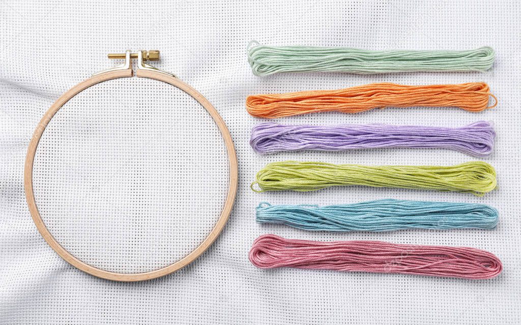 Threads near embroidery hoop with white fabric, flat lay