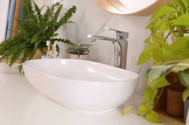 Lavabolu banyo tezgahı, beyaz mermer duvarın yanında güzel yeşil bitkiler ve diş fırçaları.