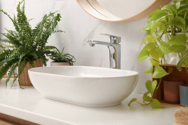 Banyo tezgahında lavabo ve beyaz mermer duvarın yanında güzel yeşil bitkiler.