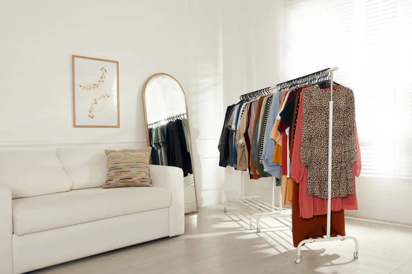 Rak Dengan Pakaian Bergaya Dekat Sofa Dan Cermin Dalam Ruangan — Stok Foto