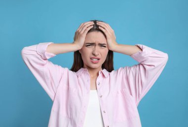 Açık mavi arka planda baş ağrısı çeken genç bir kadın.