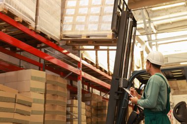 Depoda karton kutuları olan forklift kamyonunun yanında çalışan bir işçi. Lojistik kavramı
