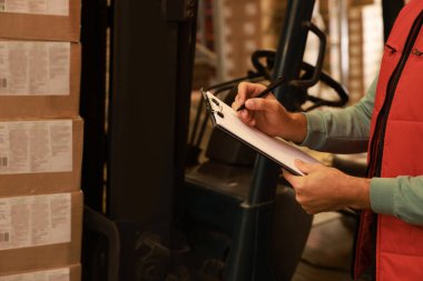 Depoda karton kutuları olan forklift kamyonunun yanındaki işçi, yakın plan. Lojistik kavramı