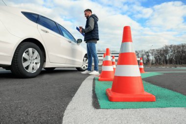 Dışarıdaki arabanın yanında panosu olan eğitmen, trafik konisine odaklan. Ehliyet sınavı