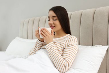 Evdeki yatakta bir bardak içkiyle güzel bir genç kadın.