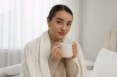 Evinde örülmüş ekoseye sarılmış bir bardak içkiyle güzel bir genç kadın.