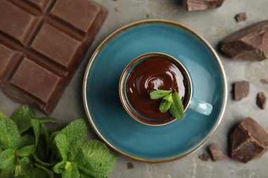 Lezzetli bir fincan sıcak çikolata, parçalar ve gri masada taze nane, düz uzanmış.