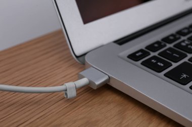 Modern laptop ve şarj kablosu ahşap masada, yakın plan.