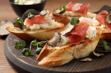 Peynirli lezzetli bruschettalar, prosciutto ve ahşap masada siyah trüf dilimleri, yakın plan.