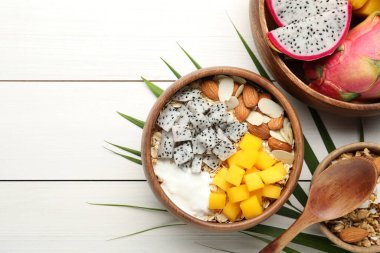 Bir kase granola, pitahaya, mango, badem ve yoğurt, beyaz ahşap masa, düz yatak. Metin için boşluk