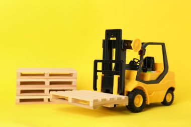 Oyuncak forklift ve sarı arkaplanda ahşap paletler
