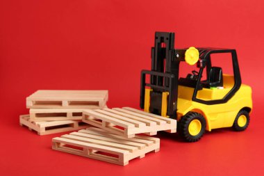 Oyuncak forklift ve kırmızı arkaplanda tahta paletler