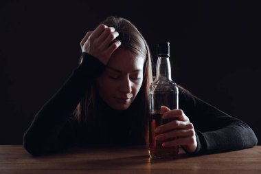 Alkol bağımlılığı. Ahşap masada elinde viski şişesi olan kadın.