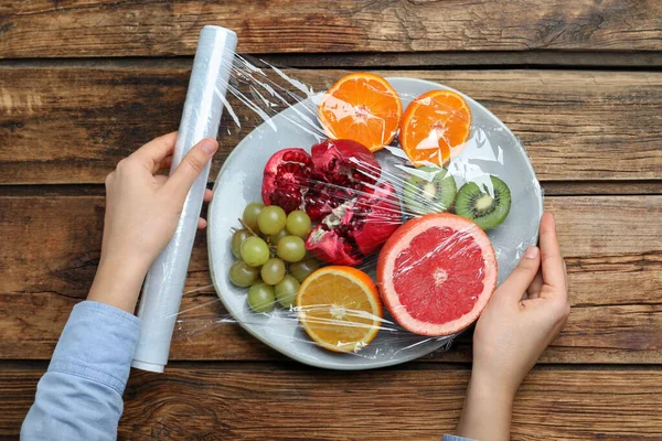 Ahşap Masada Taze Meyve Tabağının Üzerine Plastik Yiyecek Örtüsü Koyan — Stok fotoğraf