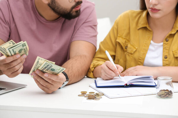 Молодая пара считает деньги за белым столом в помещении, крупным планом