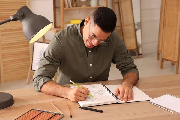 木のテーブルの上に鉛筆でスケッチブックを描く男屋内 — ストック写真