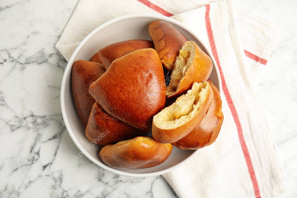 Delicious baked apple pirozhki in bowl on white marble table, flat lay