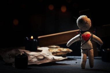 Voodoo bebeği. Karanlıkta tahta masada iğne ve tören malzemeleriyle delinmiş.