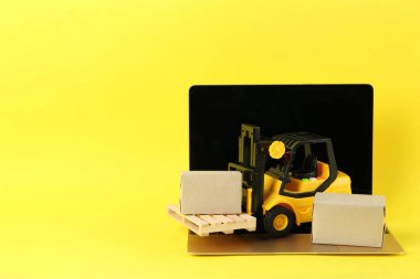 Laptop, tahta paletli oyuncak forklift ve sarı arka planda kutular, metin için boşluk