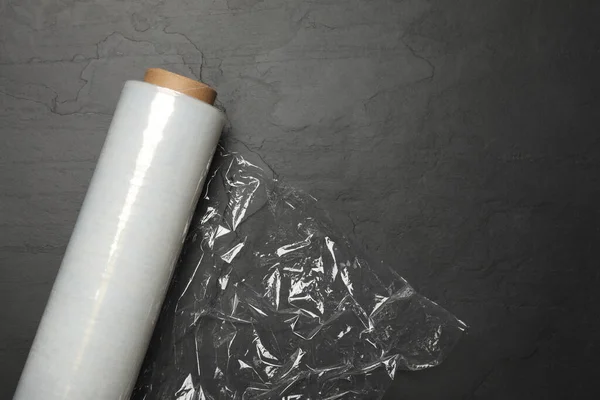 Roll of plastic stretch wrap film on black table, top view. Space for text