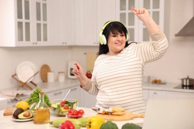 Mutfakta yemek pişirirken kulaklıkla dans eden mutlu şişman kadın.