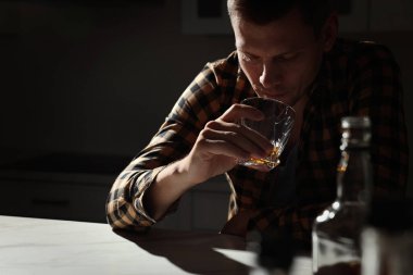 Mutfaktaki masada alkol içen bağımlı adam.