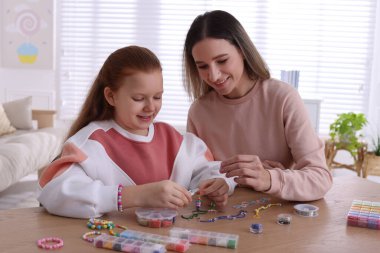 Mutlu anne ve kızı evde boncuklu mücevher yapıyorlar.