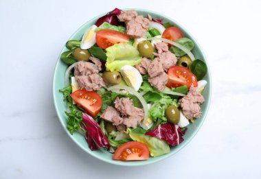 Bir kase lezzetli salata, konserve ton balığı ve sebzeler beyaz mermer masa, üst manzara.