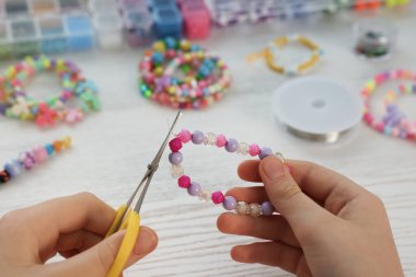 Beyaz ahşap masada boncuklu mücevher yapan kız, yakın plan.